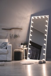 Stylish mirror with light bulbs and comfortable sofa in living room. Interior design