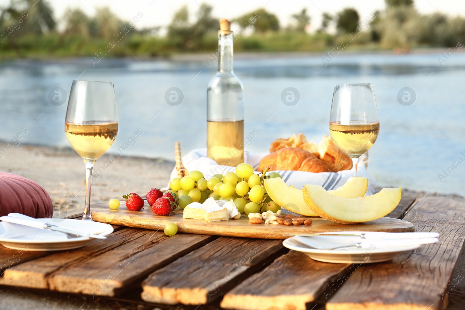 Photo of Food for picnic and white wine served on wooden pallet near river