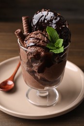Photo of Delicious chocolate ice cream with wafer sticks, donut and mint in glass dessert bowl on table, closeup
