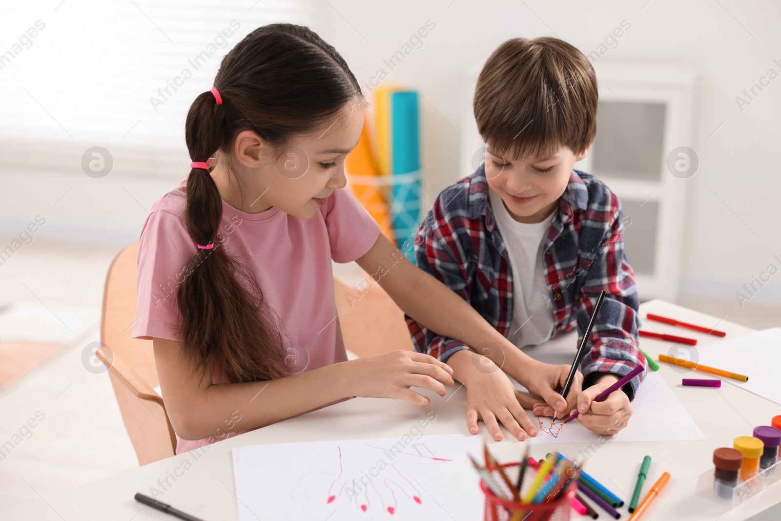 Photo of Happy brother and sister drawing at white table in room