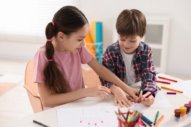 Happy brother and sister drawing at white table in room