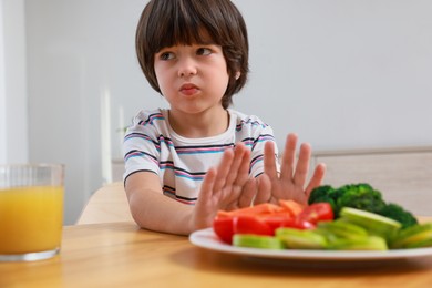 Cute little boy refusing to eat vegetables at home
