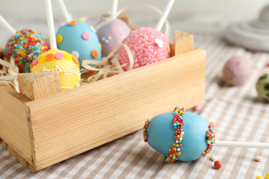 Delicious sweet cake pops in wooden crate on table, closeup. Easter holiday