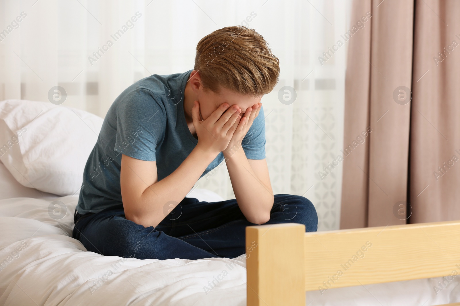 Photo of Unhappy teenage boy covering face with hands on bed at home