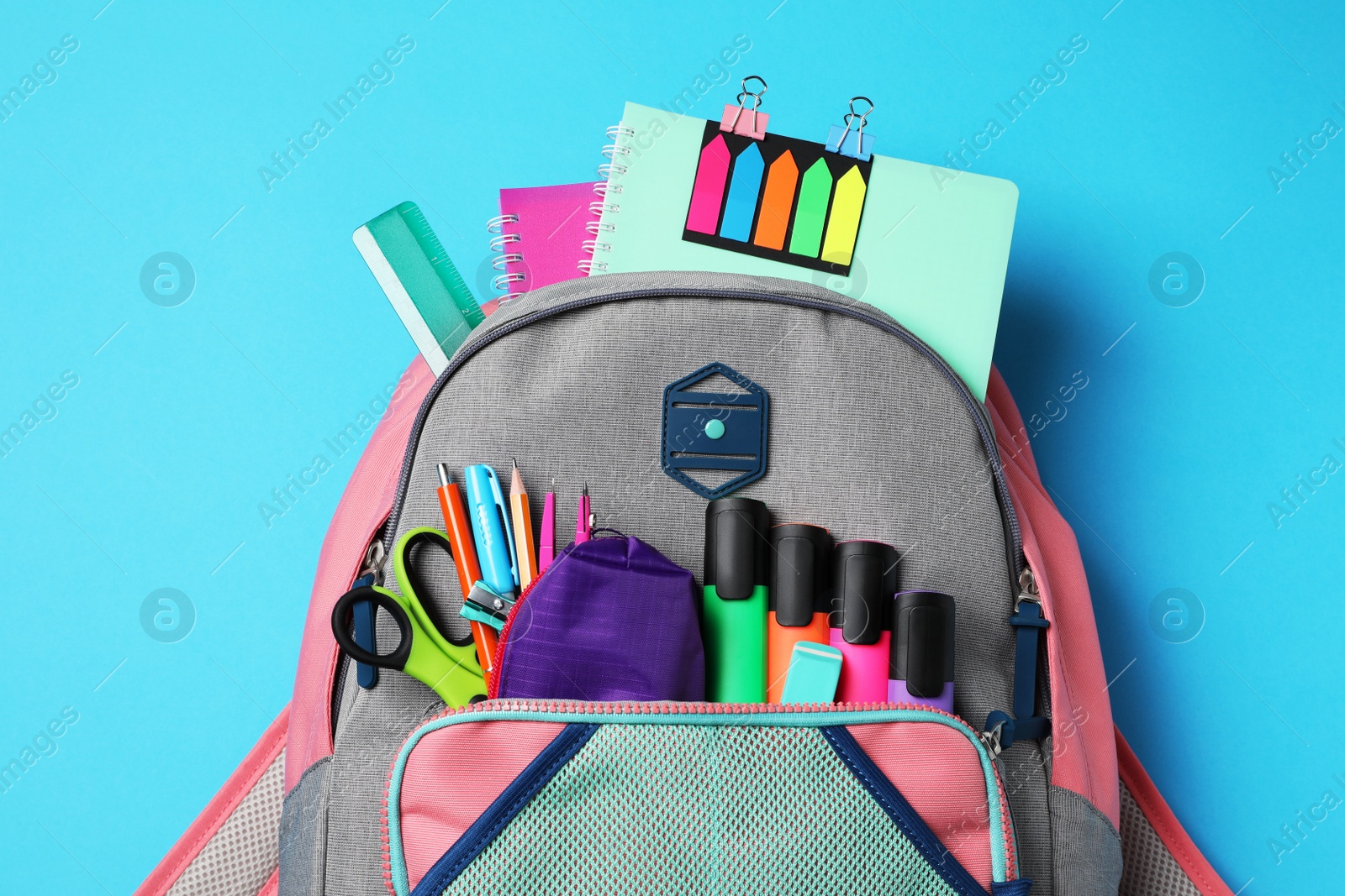 Photo of Backpack with school stationery on light blue background, top view