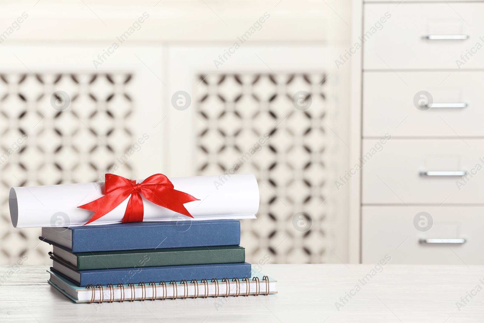 Photo of Graduate diploma with books and notebook on table against blurred background. Space for text