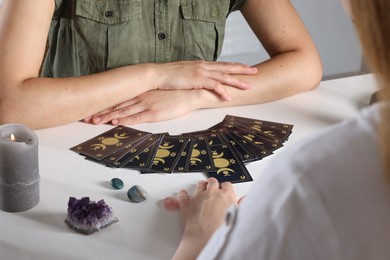 Photo of Astrologer predicting client's future with tarot cards at table indoors, closeup