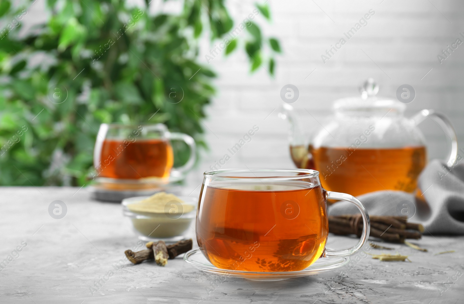 Photo of Aromatic licorice tea and dried sticks of licorice root on light gray textured table, space for text