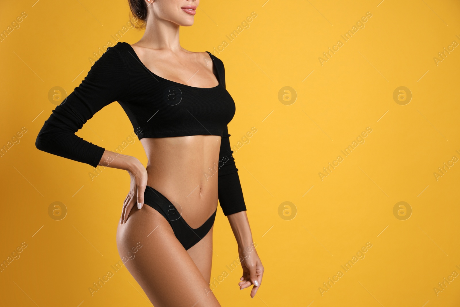 Photo of Woman in black sexy panties on yellow background, closeup. Space for text