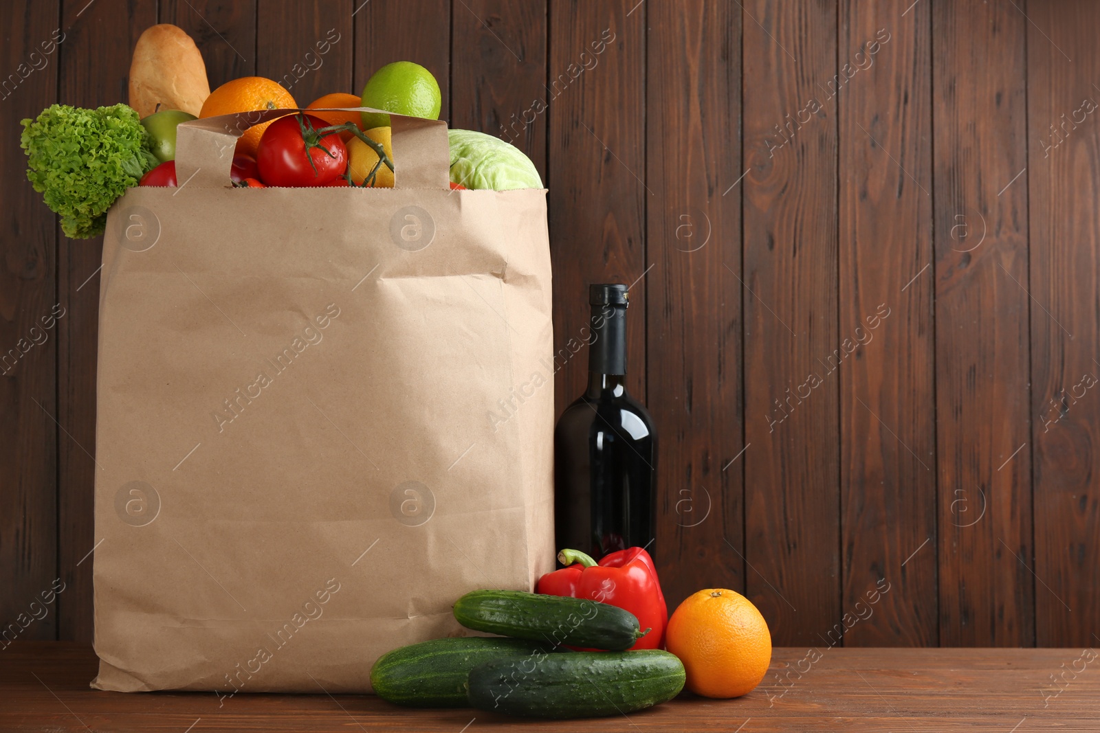 Photo of Shopping paper bag with different groceries on table against wooden background. Space for text