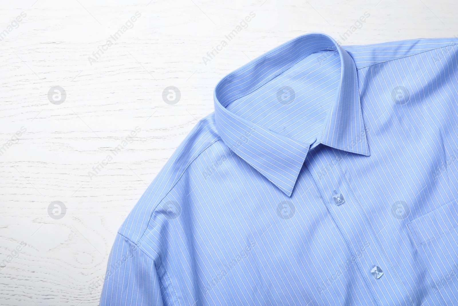 Photo of Stylish light blue shirt on white wooden table, top view. Dry-cleaning service