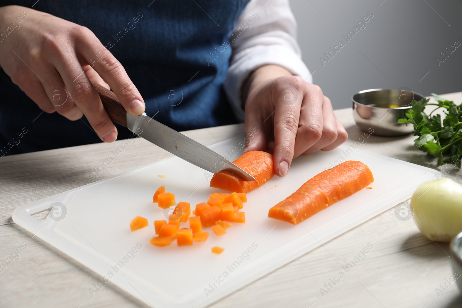 Photo of Woman cutting boiled carrot at white wooden table, closeup. Cooking vinaigrette salad