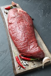 Photo of Piece of raw beef meat, garlic, chili and spices on grey textured table