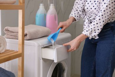 Photo of Woman pouring laundry detergent into washing machine drawer in bathroom, closeup