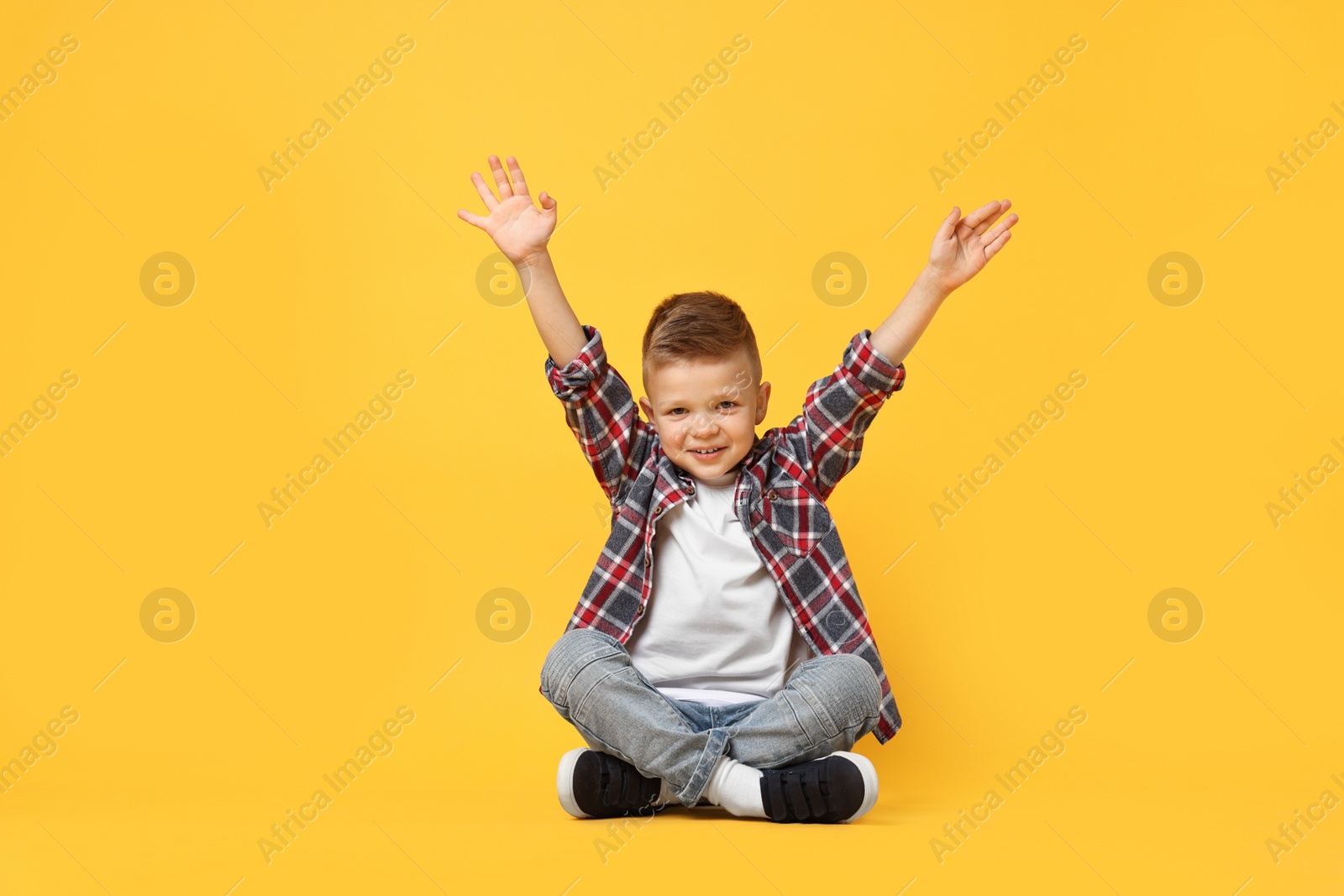 Photo of Happy little boy sitting on yellow background