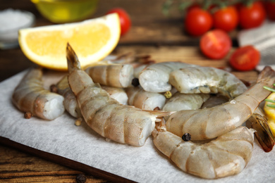 Fresh raw shrimps with lemon on wooden board, closeup