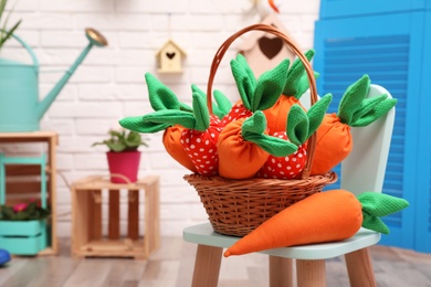 Photo of Wicker basket with cute toy carrots on chair indoors, space for text