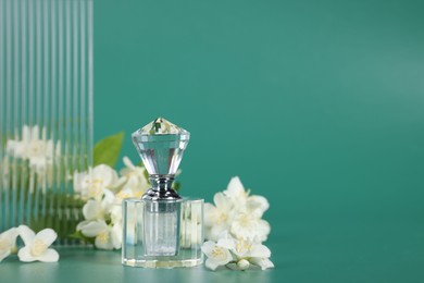 Photo of Aromatic perfume in bottle and beautiful jasmine flowers on green background, space for text