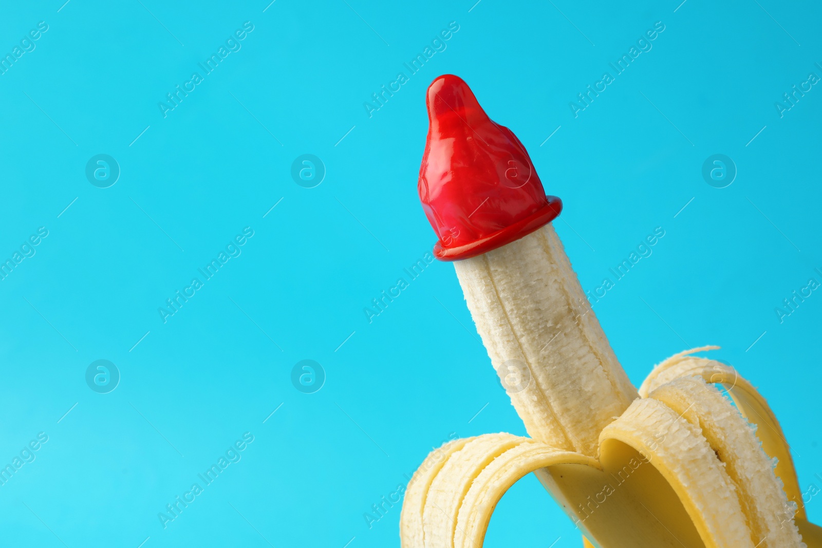 Photo of Banana with condom on light blue background, space for text. Safe sex concept