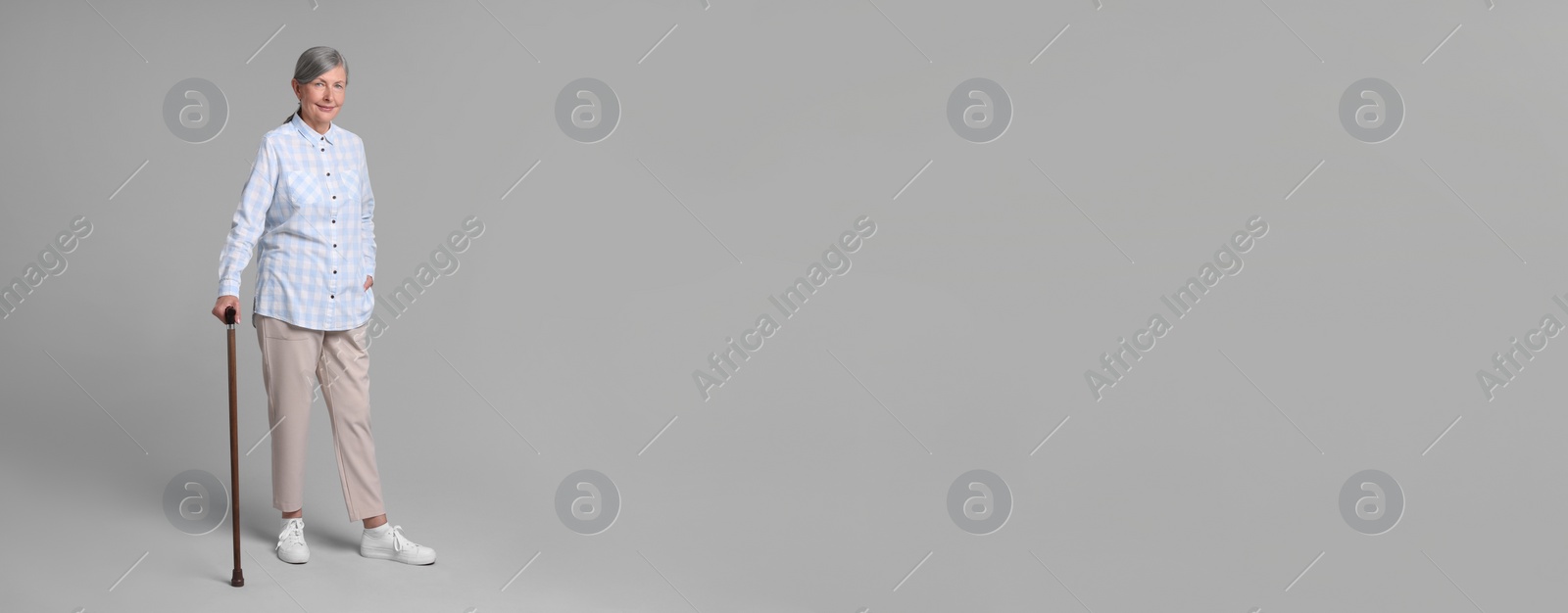 Image of Senior woman with walking cane on gray background. Banner design with space for text