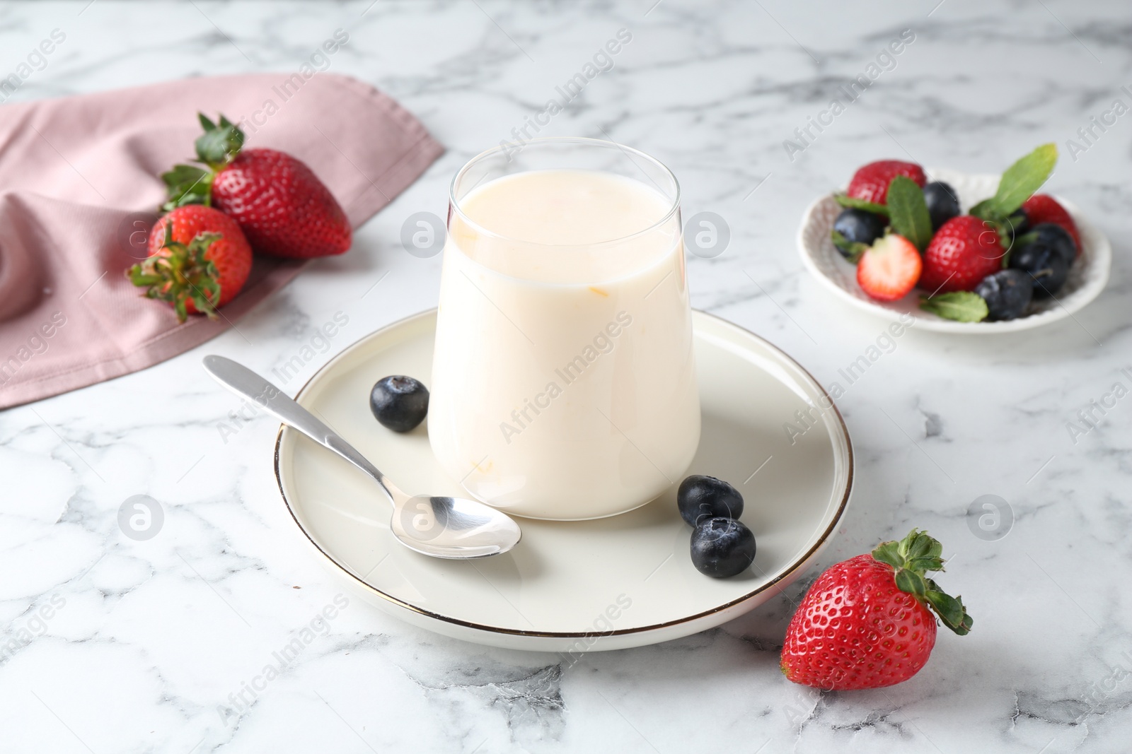 Photo of Tasty yogurt in glass and berries on white marble table