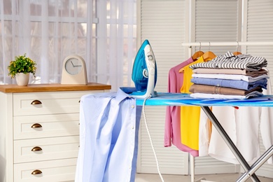 Photo of Stack of clean clothes and iron on board indoors