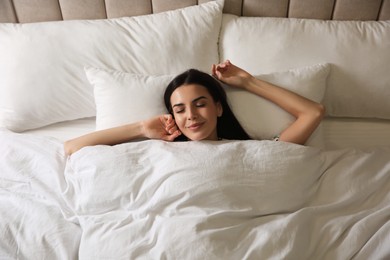 Photo of Young woman sleeping in bed covered with white blanket, top view