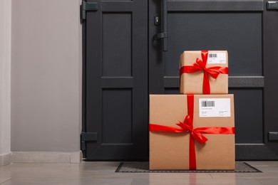 Photo of Christmas gift boxes on floor near door, space for text. Sending present by mail
