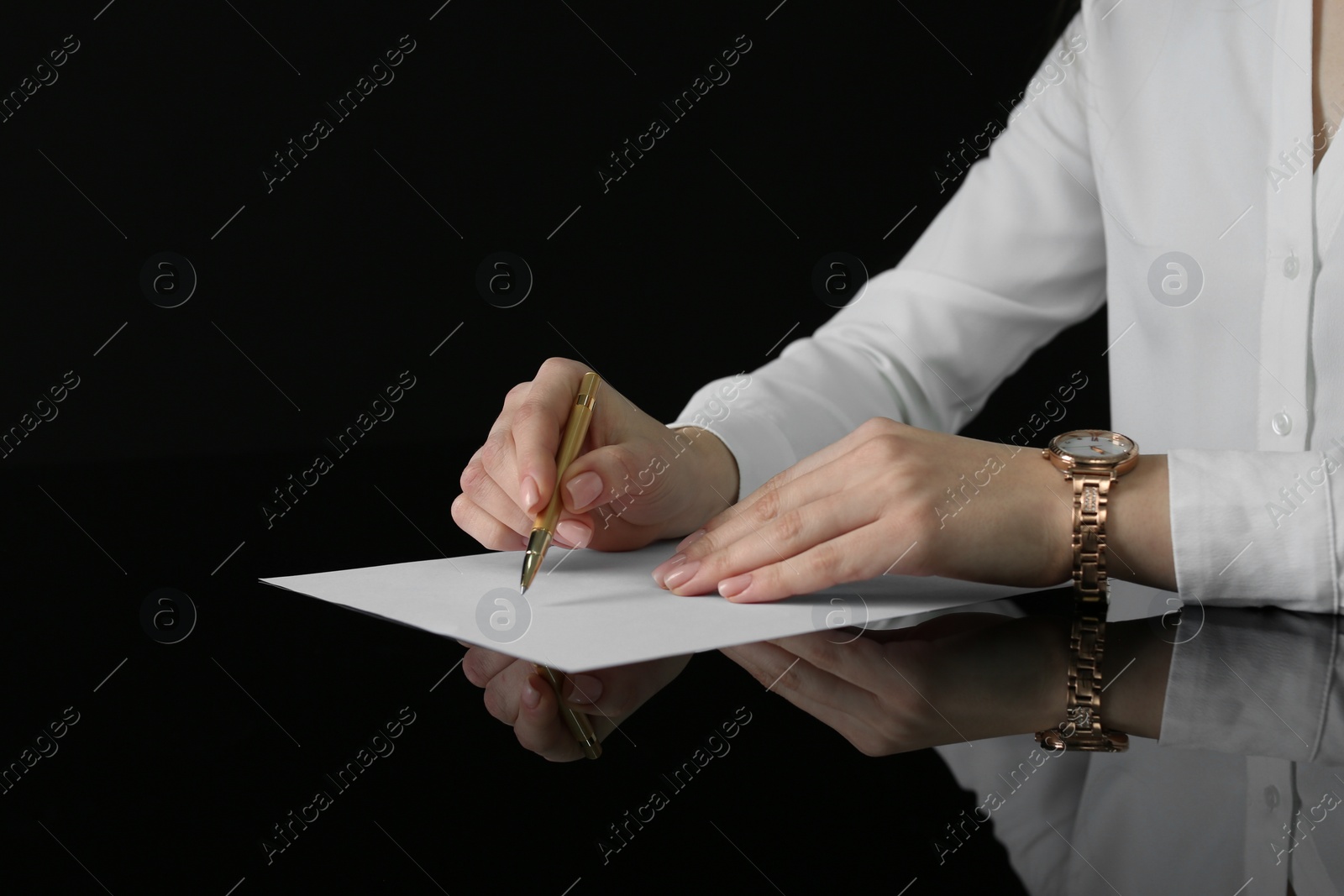 Photo of Woman writing on sheet of paper at glass table, closeup