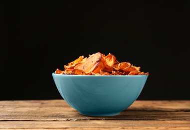 Photo of Bowl of sweet potato chips on table against black background. Space for text