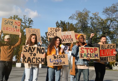 Photo of Protesters demonstrating different anti racism slogans outdoors. People holding signs with phrases