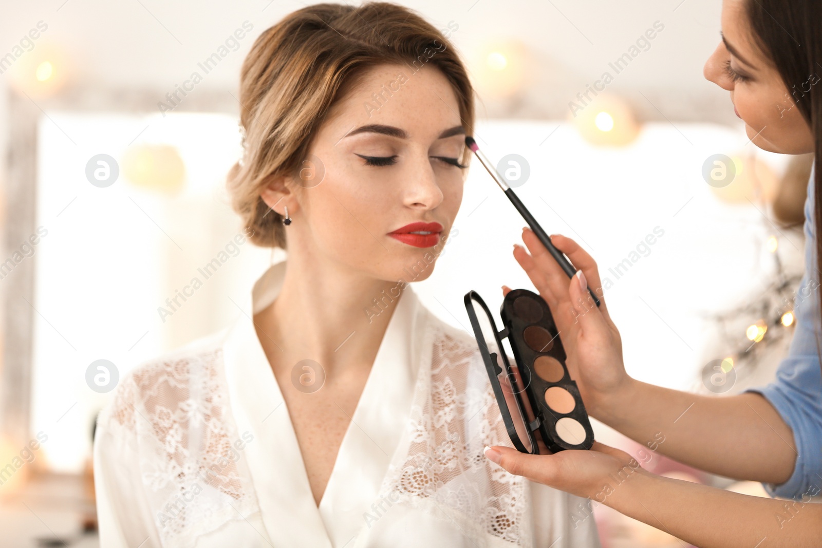 Photo of Makeup artist preparing bride before her wedding in room