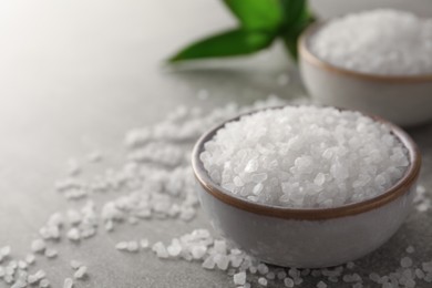 Bowls of natural sea salt on grey table, closeup. Space for text