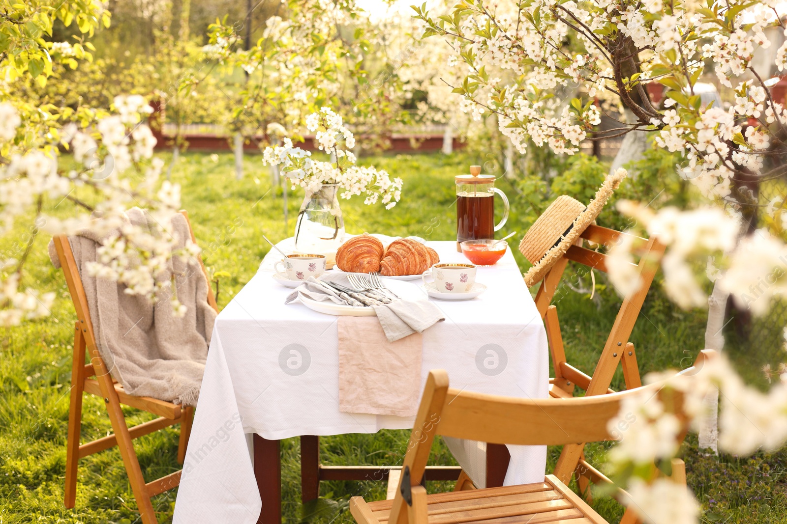 Photo of Stylish table setting with beautiful spring flowers, tea and croissants in garden