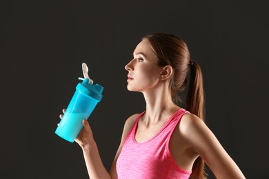 Photo of Athletic young woman drinking protein shake on black background
