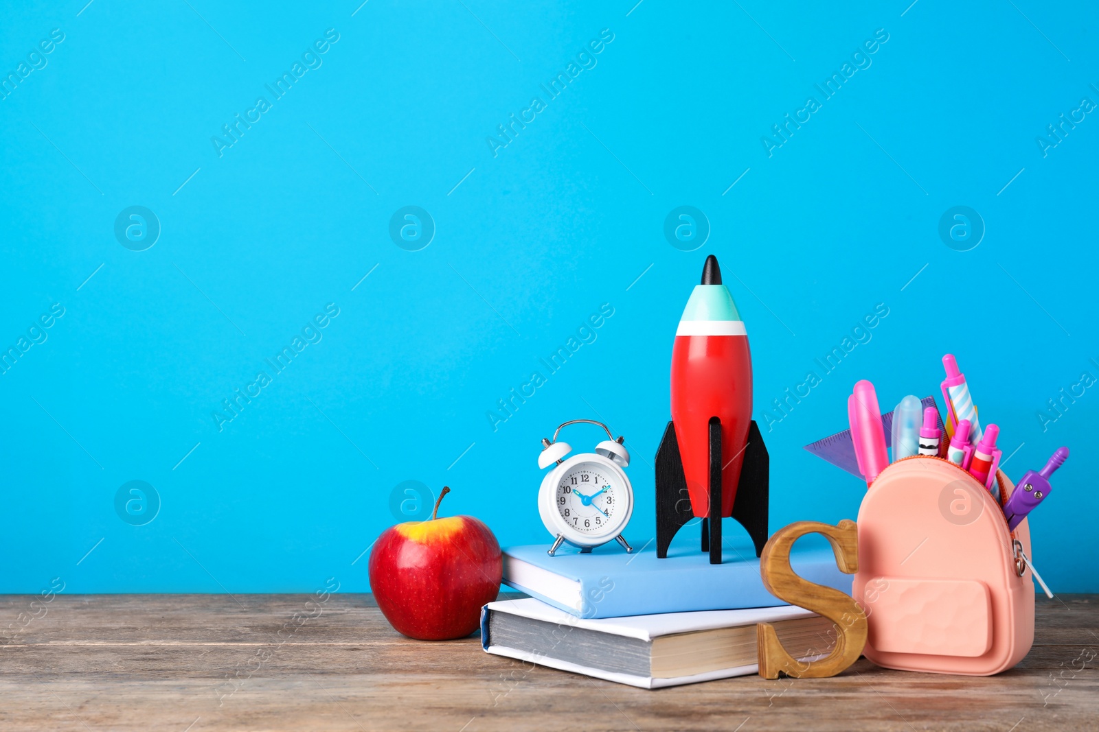 Photo of Bright toy rocket and school supplies on wooden desk. Space for text