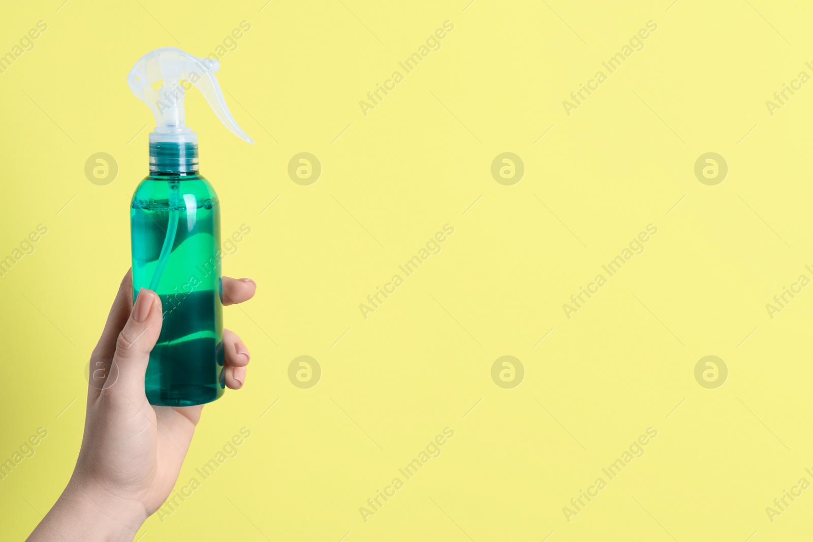 Photo of Woman holding spray bottle with hair thermal protection against pale yellow background, closeup. Space for text