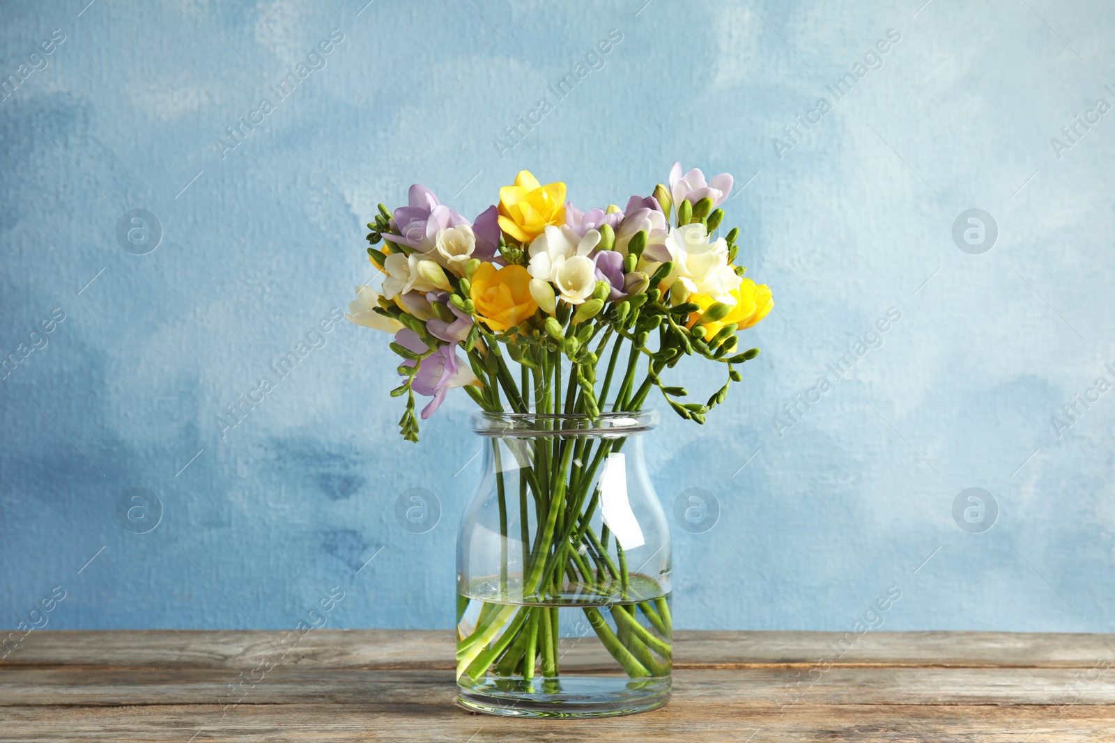 Photo of Bouquet of fresh freesia flowers in glass vase on table