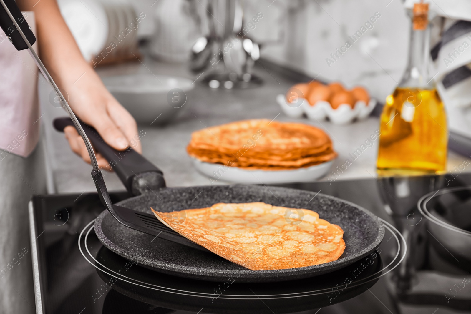 Photo of Woman cooking delicious thin pancakes on induction stove, closeup