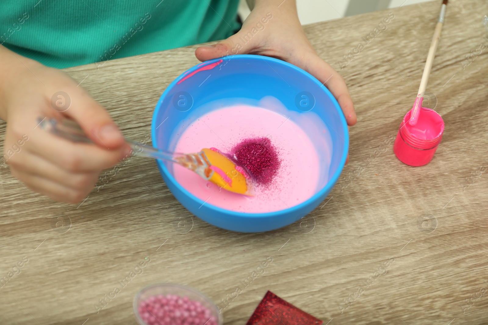 Photo of Little girl mixing ingredients with silicone spatula at table, closeup. DIY slime toy