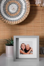 Frame with photo of elderly woman and her granddaughter on white table indoors