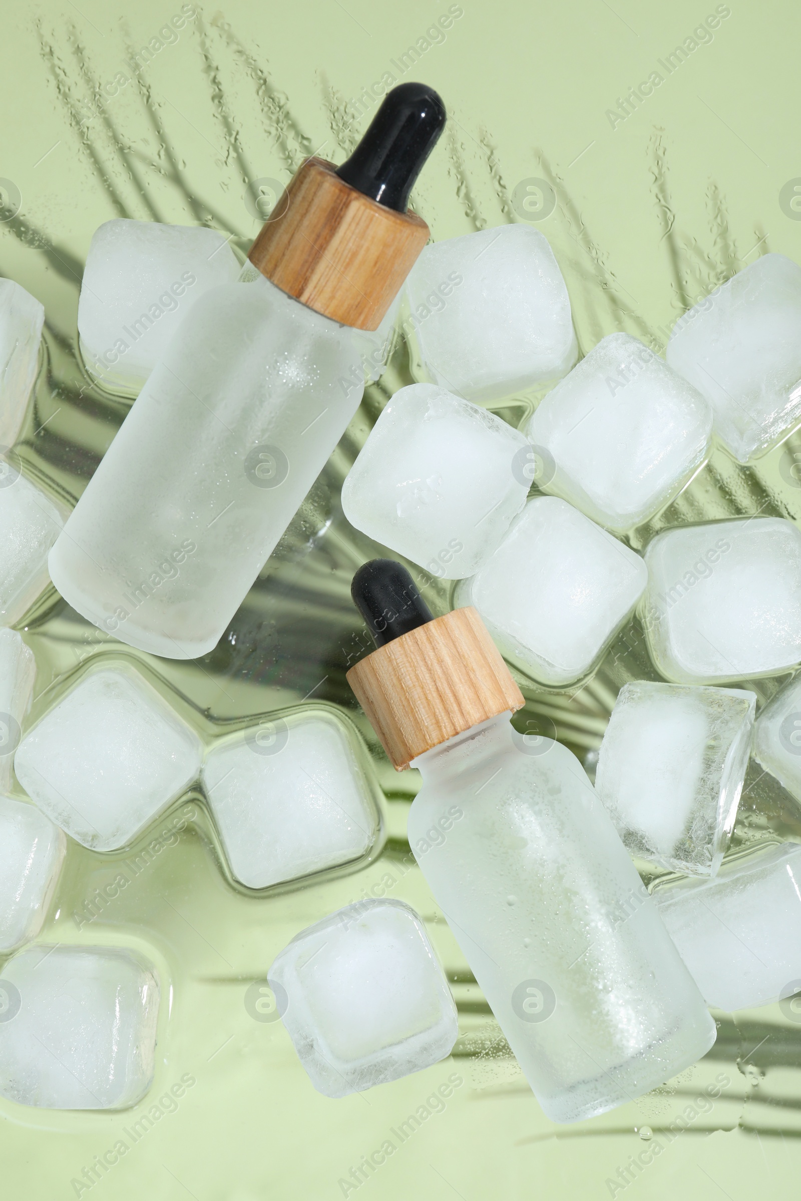 Photo of Bottles of cosmetic product and ice cubes on glass surface, flat lay