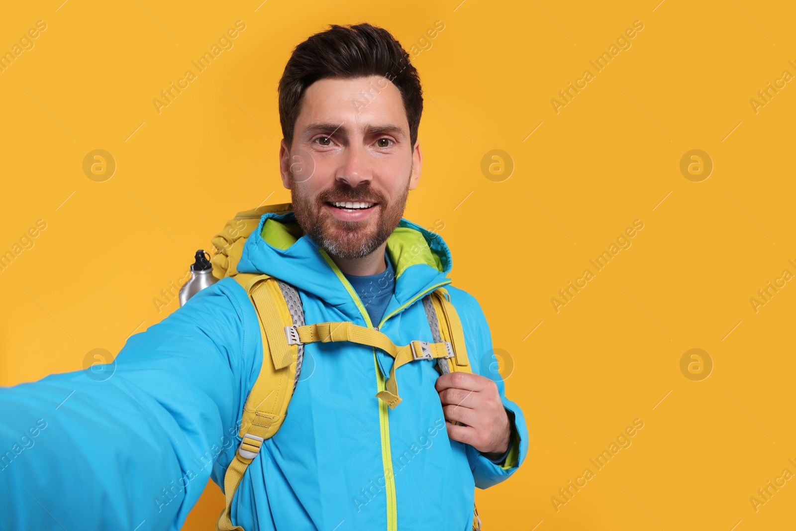 Photo of Happy man with backpack taking selfie on orange background, space for text. Active tourism