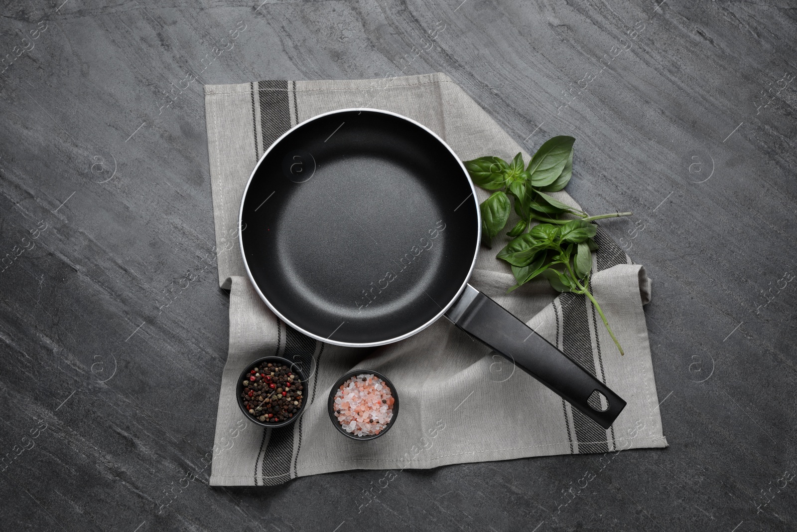 Photo of Frying pan, basil and spices on grey table, top view