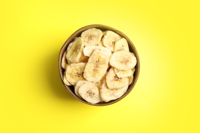 Photo of Wooden bowl with sweet banana slices on color background, top view. Dried fruit as healthy snack