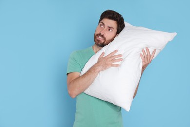 Photo of Smiling handsome man hugging soft pillow on light blue background