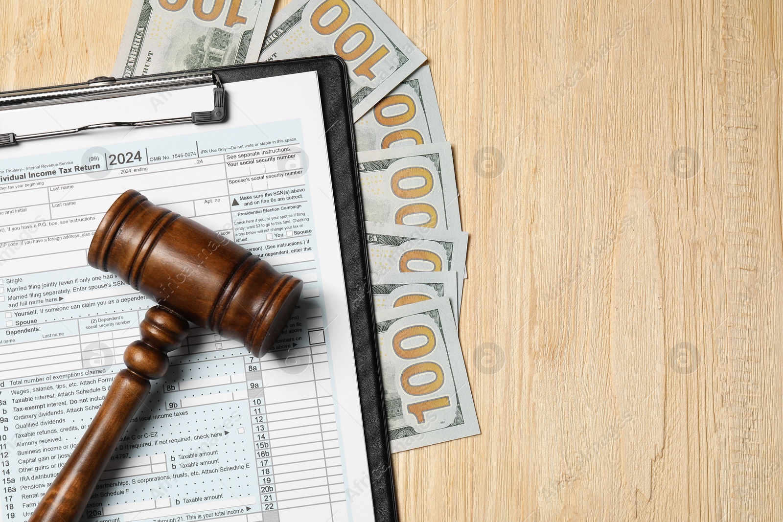 Photo of Clipboard with tax return form, gavel and dollar banknotes on wooden table, flat lay. Space for text