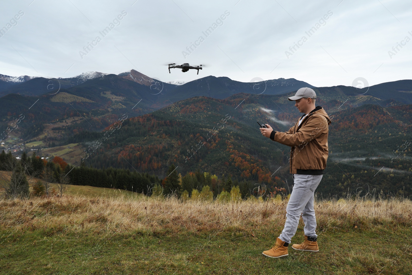 Photo of Young man operating modern drone with remote control in mountains