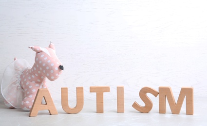 Photo of Word AUTISM and toy dog on table against light background