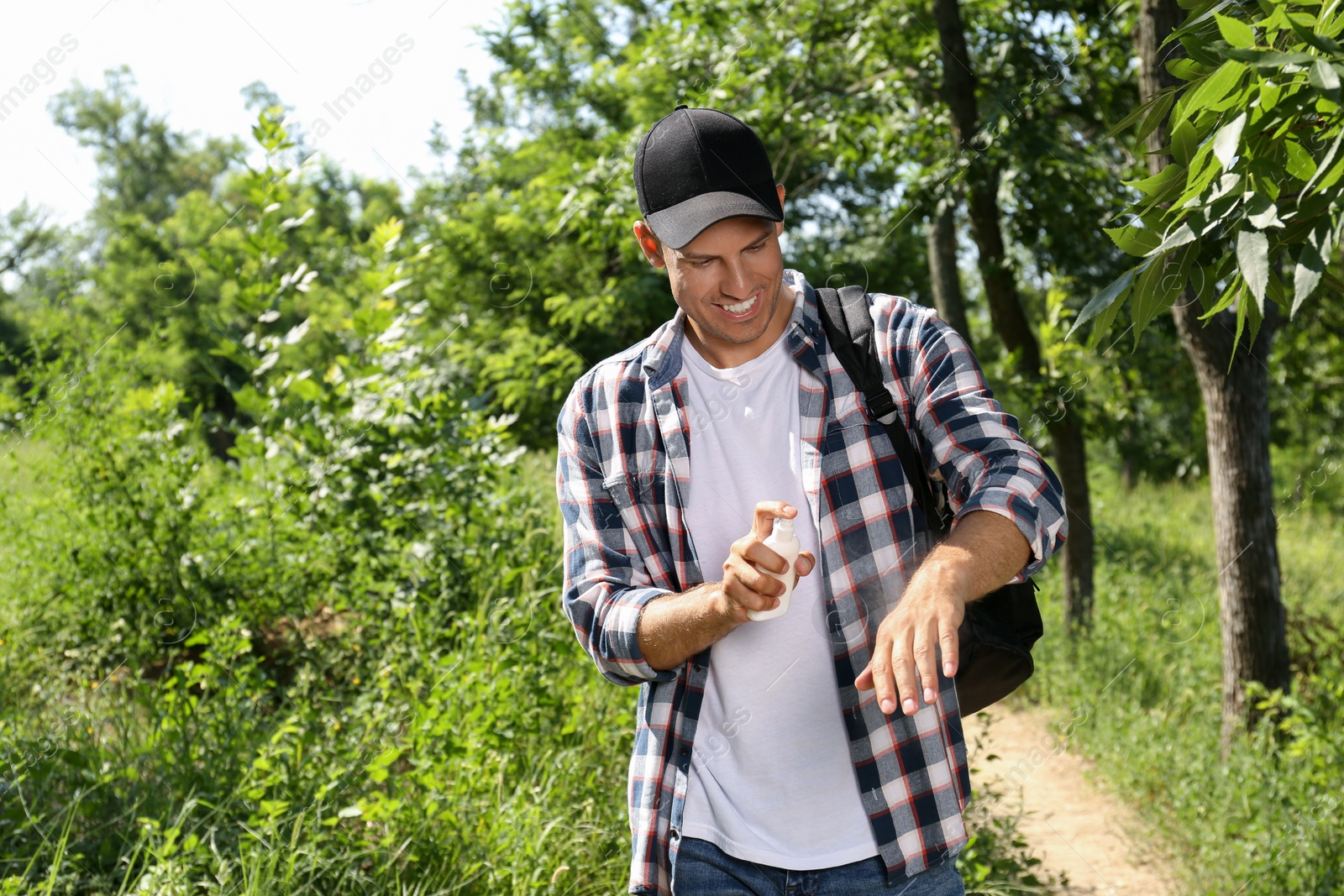 Photo of Man spraying tick repellent on arm during hike in nature